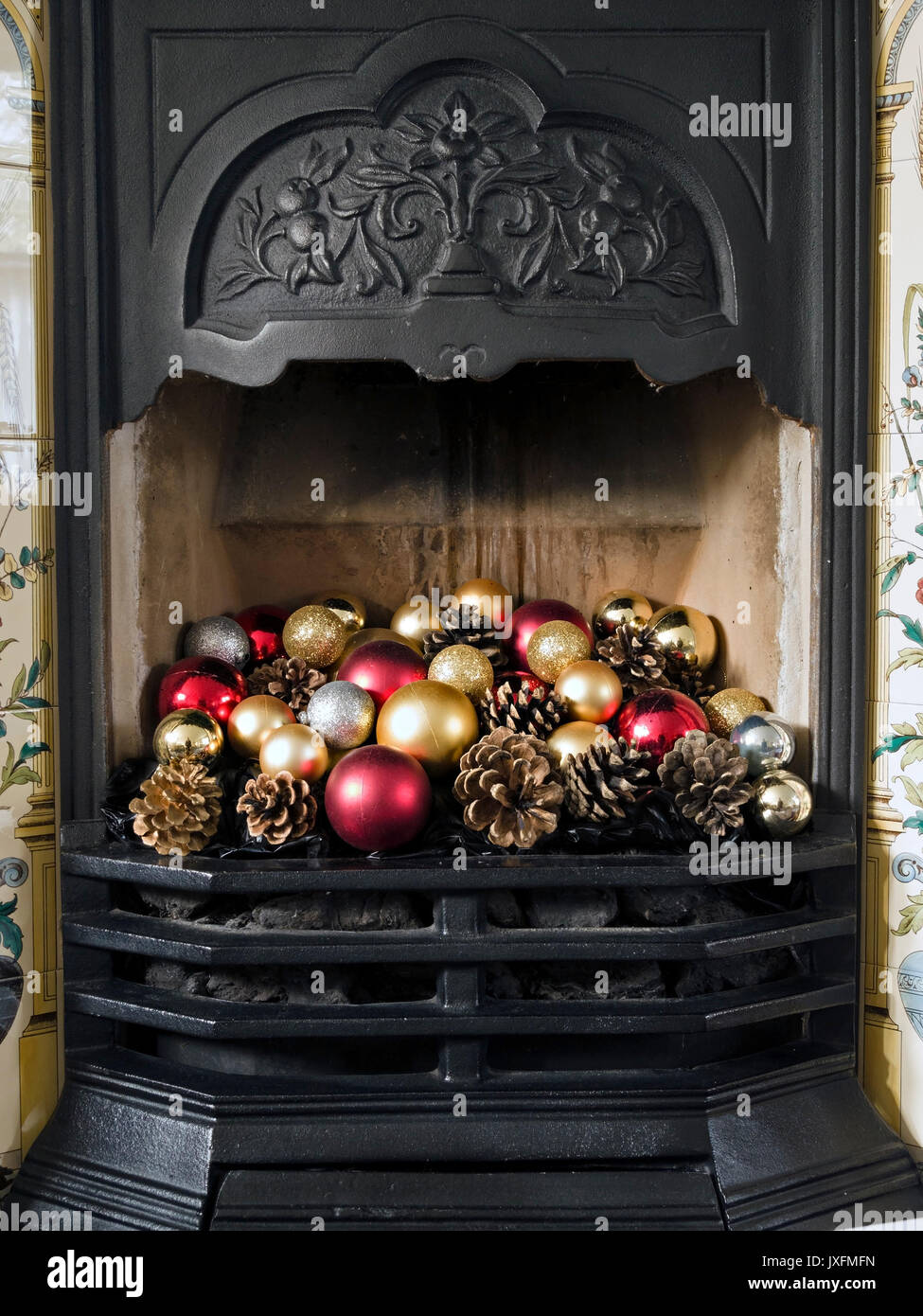 Hübscher, gusseiserner Kamin im viktorianischen Stil mit farbenfrohen Weihnachtskugeln und Tannenzapfen, England, Großbritannien Stockfoto