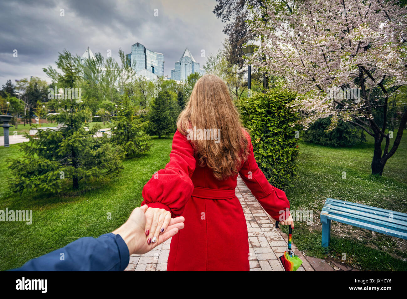 Frau im roten Mantel und Schirm halten sie ihre Freundin und führt zu der Stadtpark mit Cherry Blossom und bedecktem Himmel Stockfoto