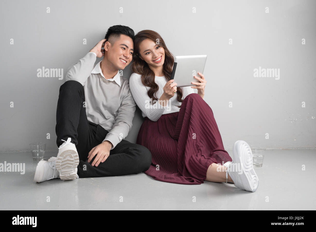 Ziemlich lächelnde asiatische paar in Liebe zusammen sitzen im Stock genießen Sie mit digital-Tablette Stockfoto