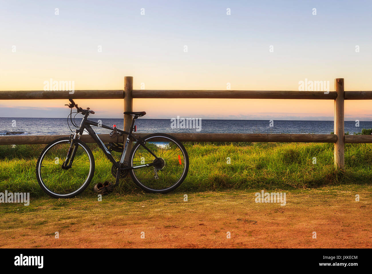 Schwarz moderne Sport Fahrrad an der hölzernen Pfosten der Zaun am leeren Strand bei Sonnenaufgang gesichert. Stockfoto