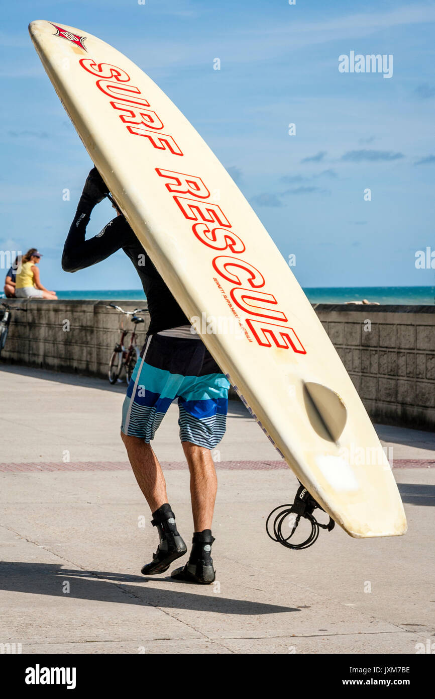 Ein Mann nimmt sein Surfbrett am Strand, Rottingdean, East Sussex, Großbritannien Stockfoto