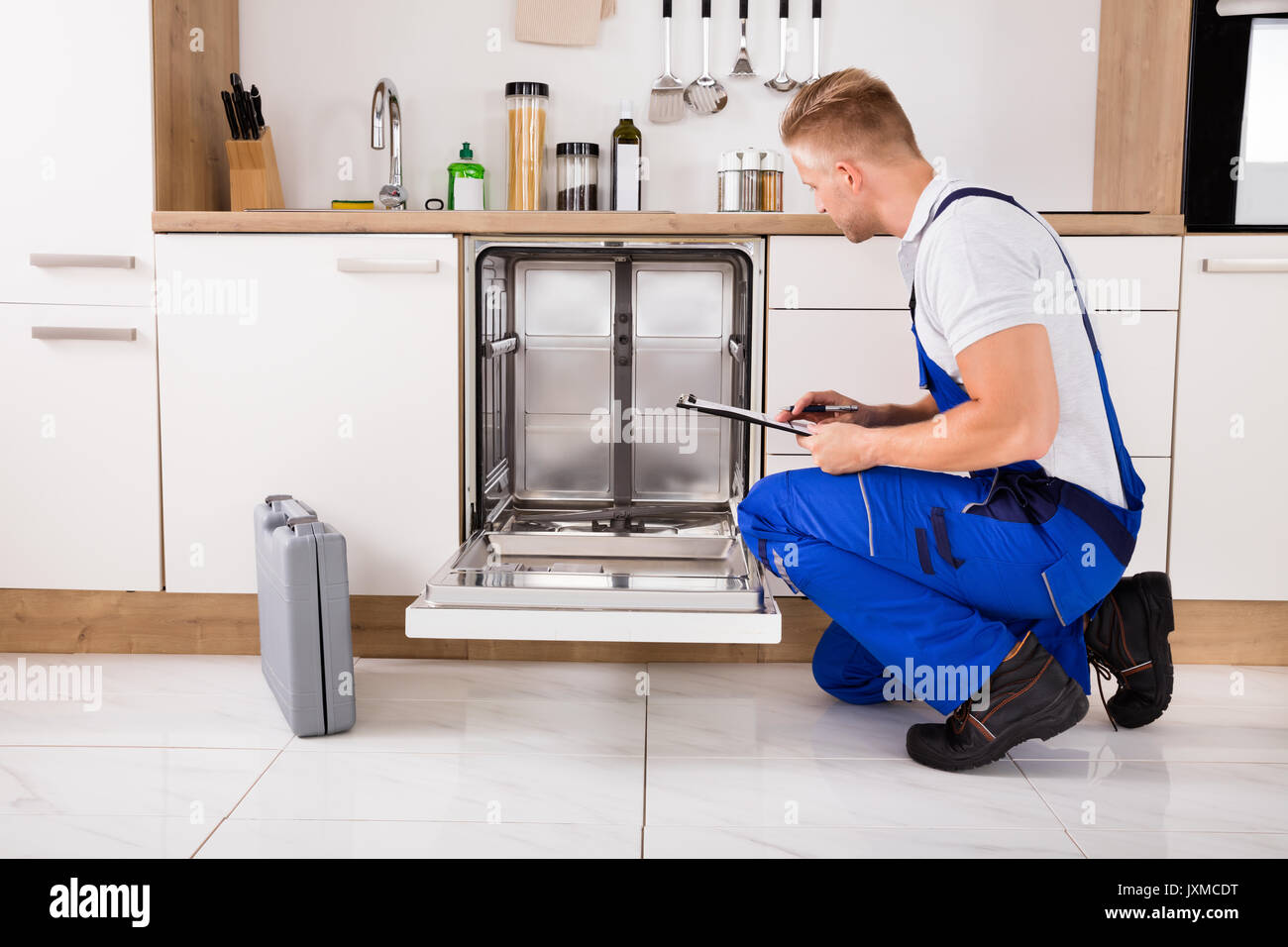 Handwerker in der Nähe Spülmaschine schriftlich über die Zwischenablage in der Küche Stockfoto