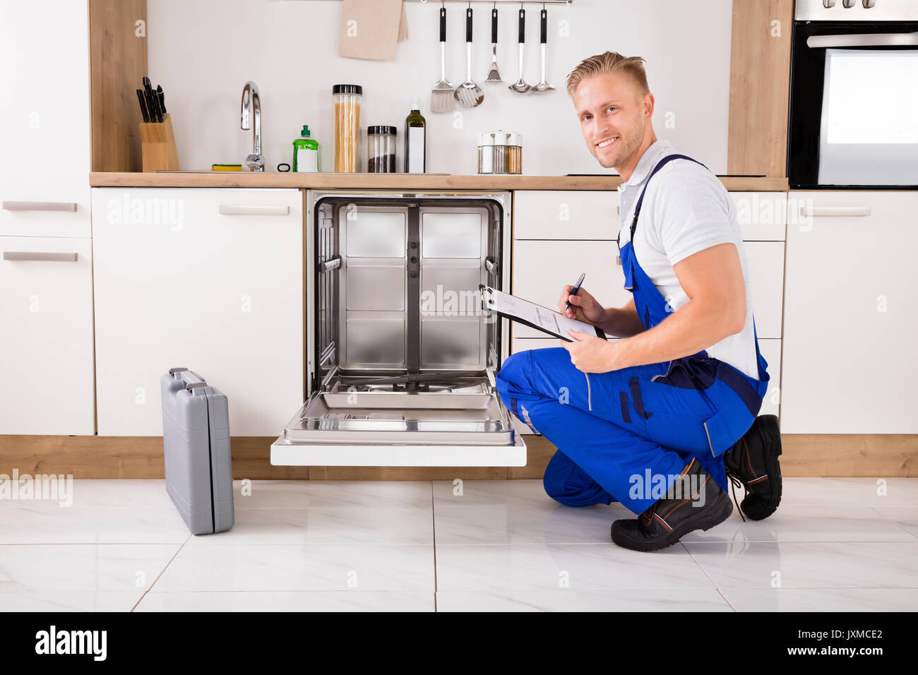 Handwerker in der Nähe Spülmaschine schriftlich über die Zwischenablage in der Küche Stockfoto