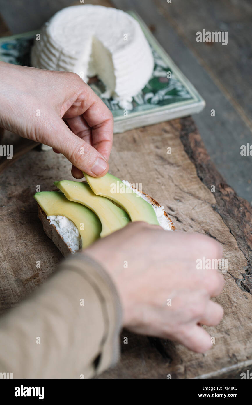 Frau Inverkehrbringen Scheiben Avocado auf geschnittenes Brot mit Ricotta, close-up Stockfoto