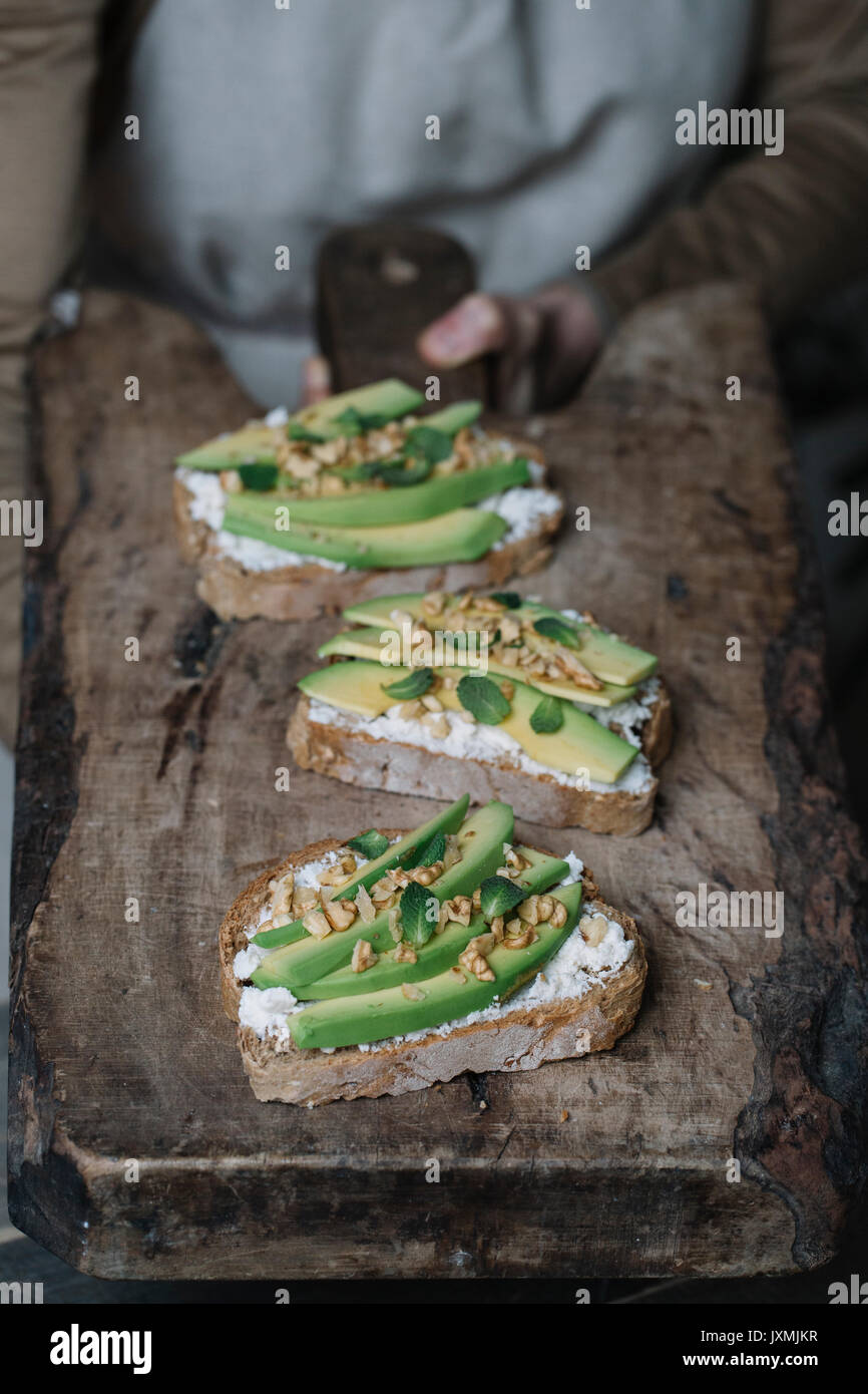 Frau mit Schneidebrett, mit Ricotta, Avocado und Nussbaum bruschetta auf der Oberseite, close-up Stockfoto