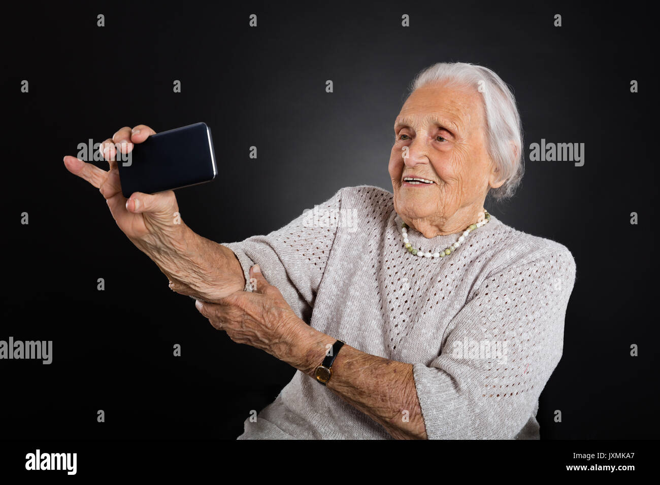 Portrait von lächelnden ältere Frau unter Selfie mit Smartphone über grauer Hintergrund Stockfoto