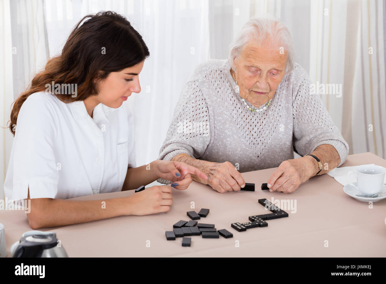 Ältere Frau spielen Domino Spiel auf Tabelle mit ihrer Amme im Krankenhaus Stockfoto