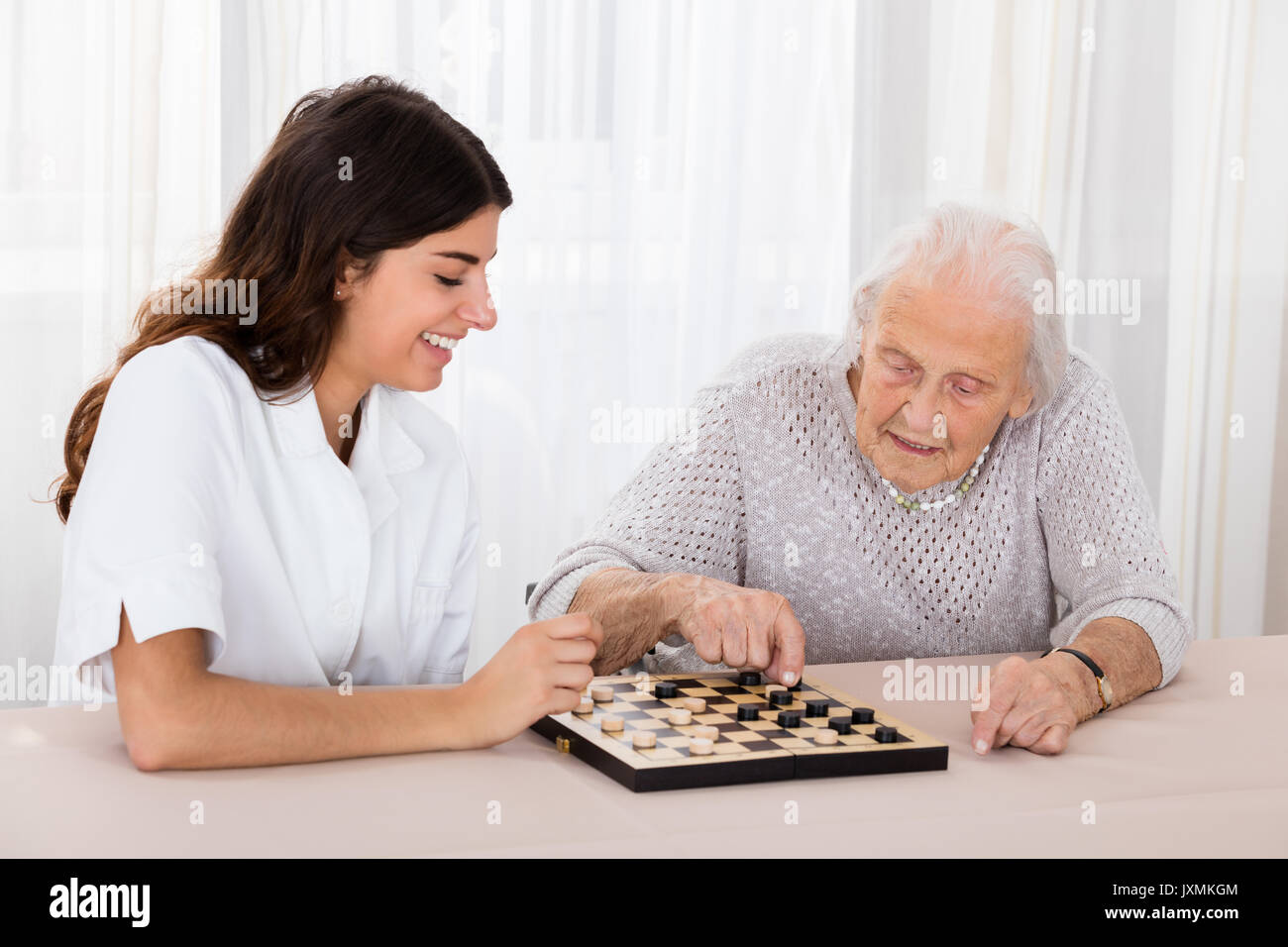 Ältere Frau spielen Checkers Spiel Mit junge Krankenschwester auf Tisch Stockfoto