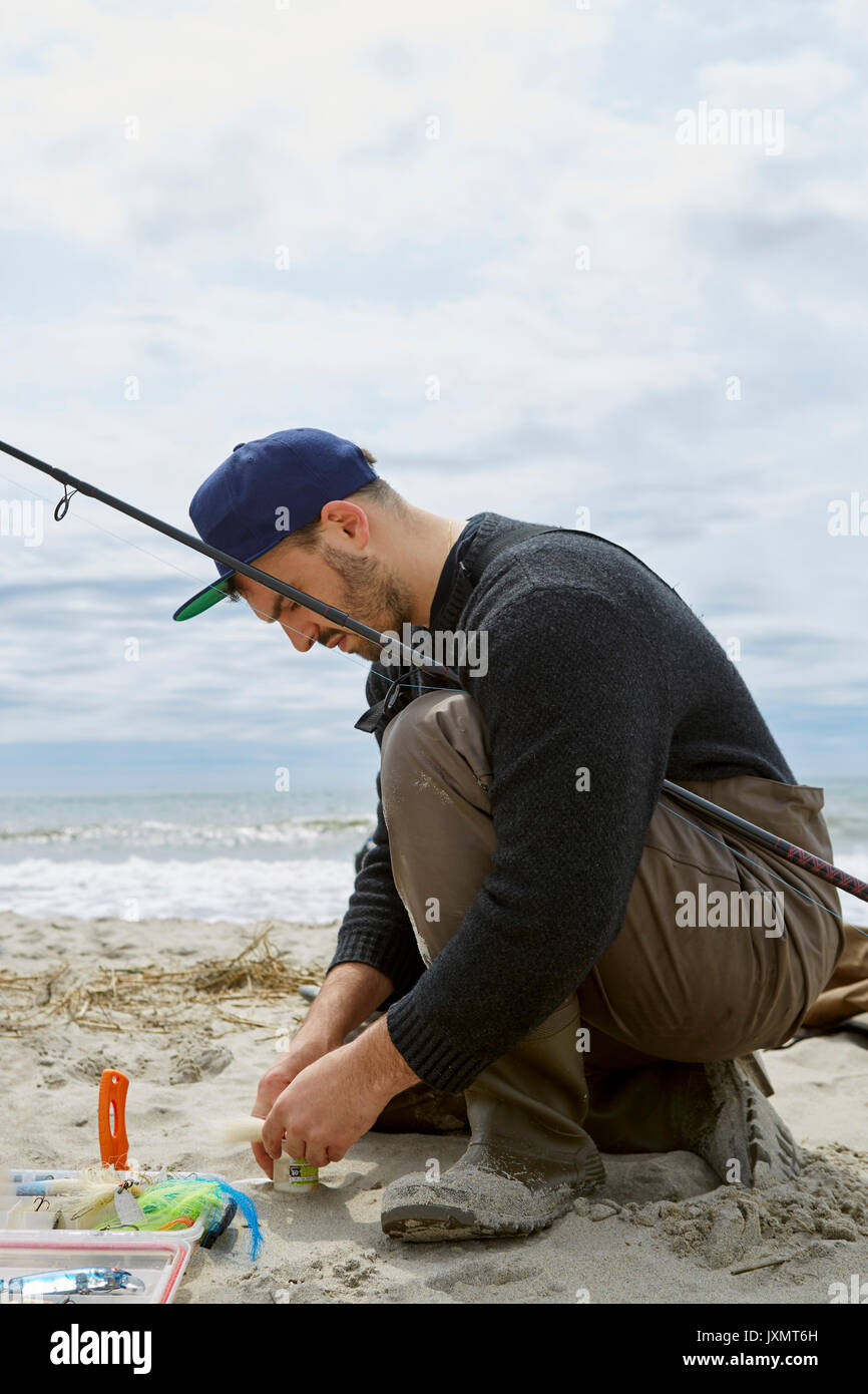 Kauernden jungen Mann Vorbereitung angeln Haken am Strand Stockfoto