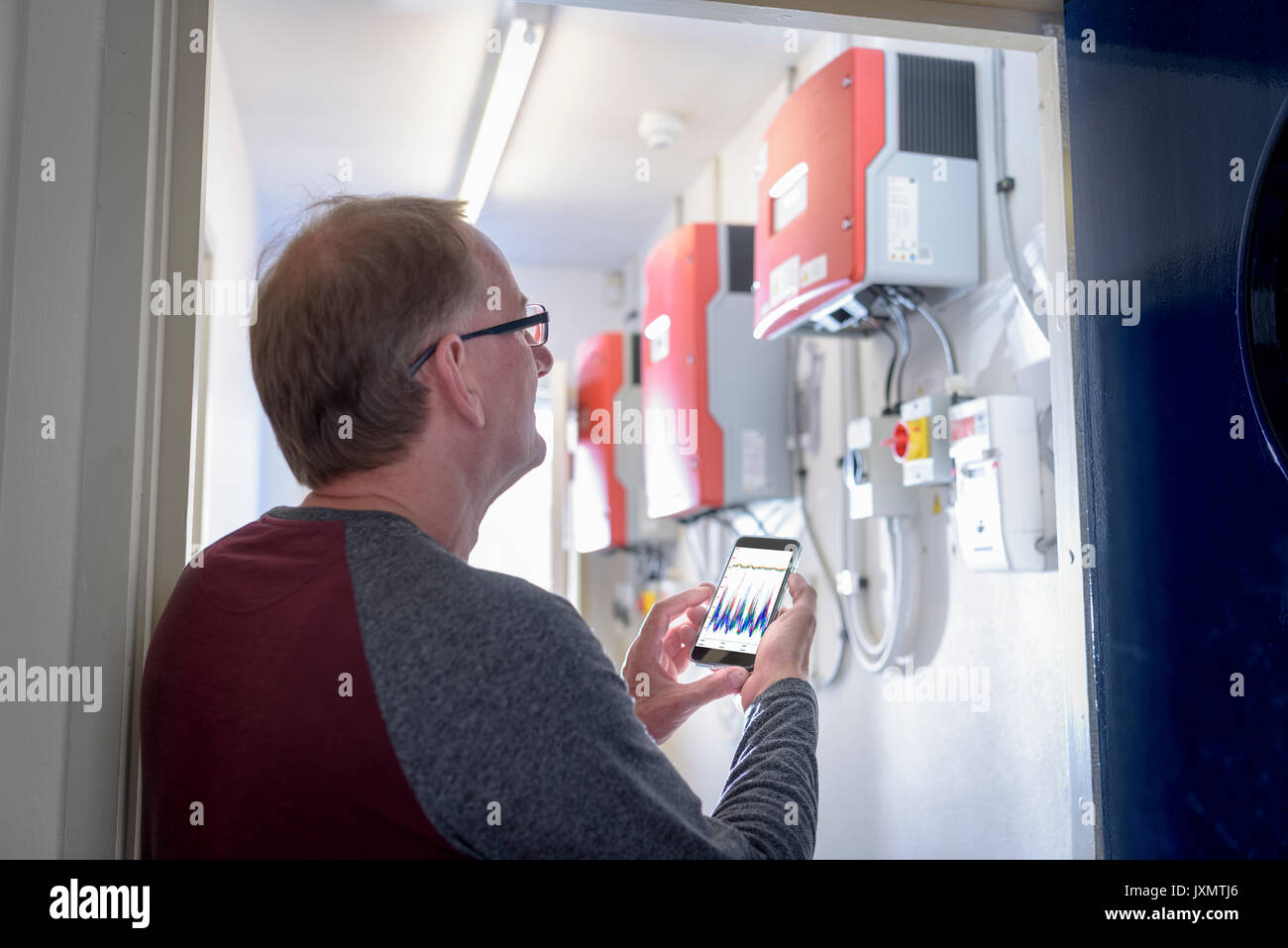 Arbeitnehmer aus der Gemeinschaft mit Smartphone App Wärmepumpe Energie Kontrollen zu prüfen. Stockfoto