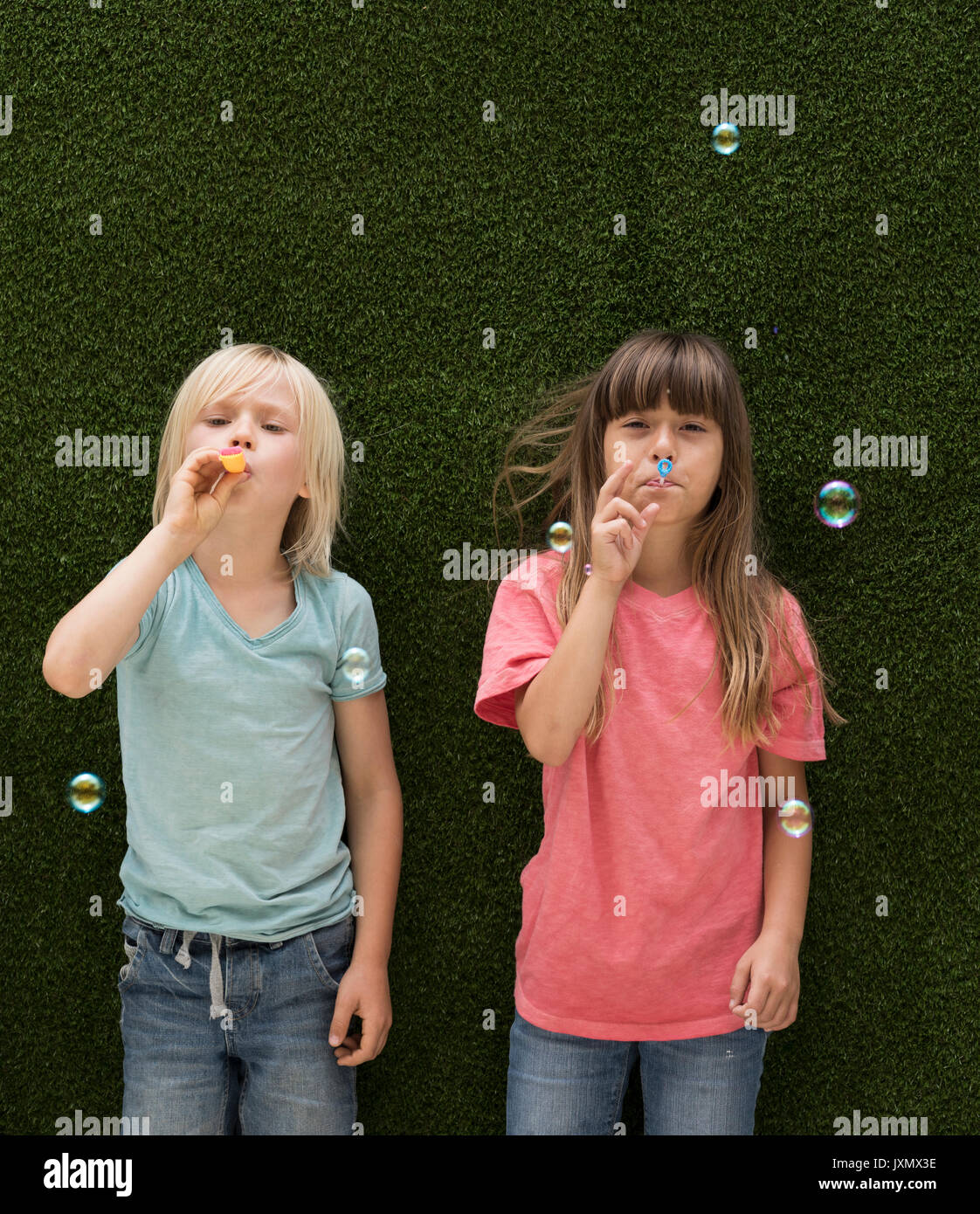 Kinder vor der Kunstrasen Wand bläst Seifenblasen Stockfoto