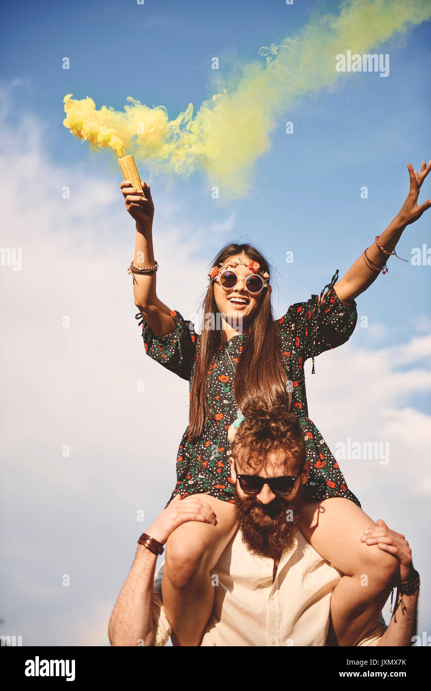 Junge boho Frau mit gelben Rauch flare auf Freund Schultern bei Festival Stockfoto