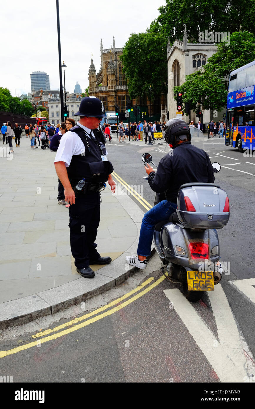 Ein Polizist im Dienst an den Toren zu den Häusern von Parliamrnt in London, wird eine geparkte Mopedfahrer auf sich zu bewegen Stockfoto