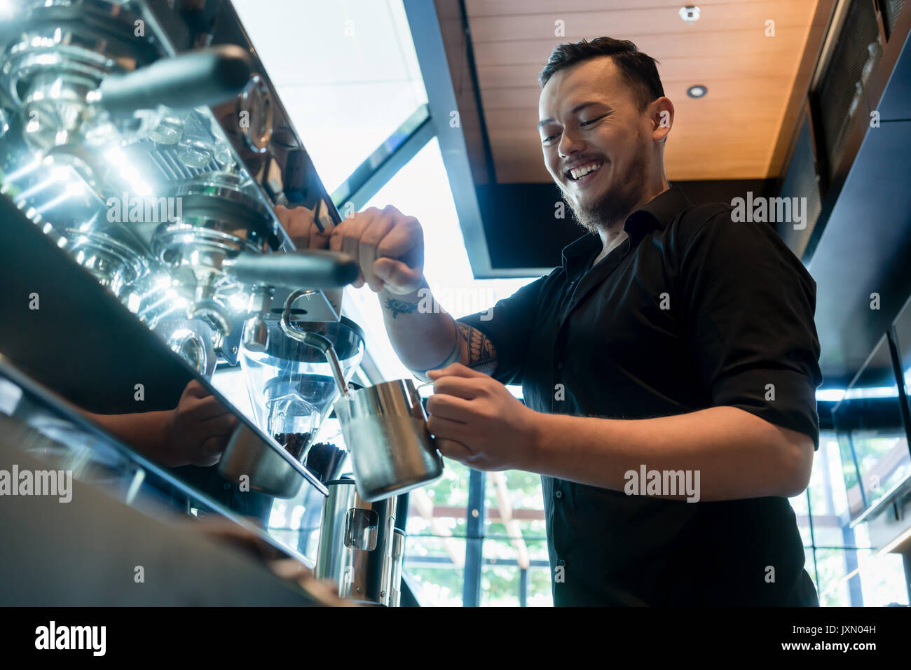 Junge fröhliche barista Vorbereitung auf eine automatische Maschine Stockfoto