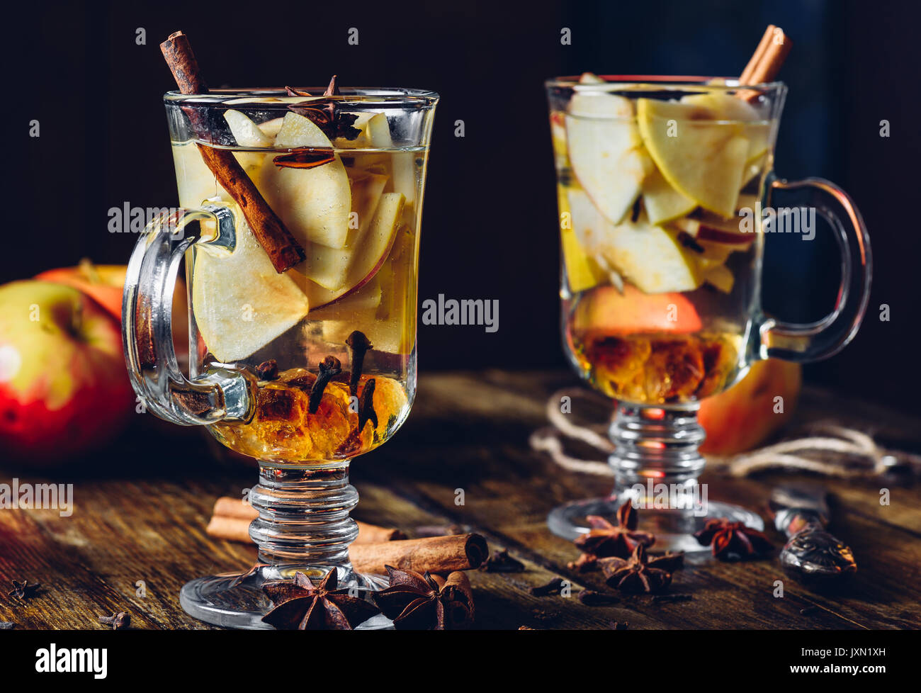 Zwei Gläser Weihnachten gewürzte Getränke mit in Scheiben geschnittenen Apfel, Nelke, Zimt, Anis Sterne und Dunkle Kandiszucker. Alle Zutaten und einige Küchengeräte Stockfoto