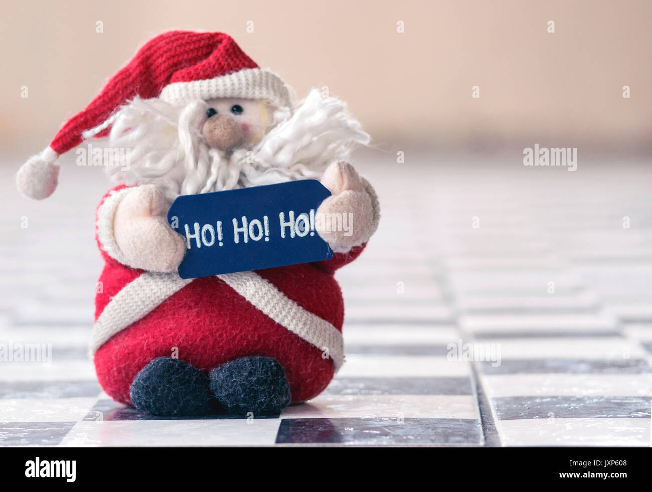 Santa Claus, gefüllte flauschige Spielzeug, rot tragen, mit einem Bart und Hut mit einem Schild geschrieben, Ho Ho Ho, auf einem schwarz-weißen Fliesenboden, mit extra kopieren Stockfoto