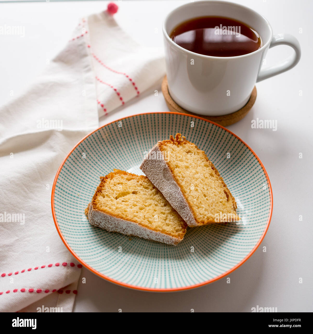 Tasse Kaffee und zwei Scheiben Biskuit in einer Platte auf einem weißen Tisch mit einem weißen und roten Küchenhandtuch. Ansicht von oben. Quadratisches Format. Stockfoto