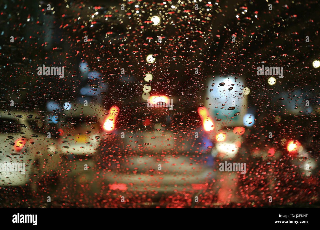 Verschwommen Straßenlaternen und Rückleuchten durch die Regentropfen auf dem Auto Windschutzscheibe bei Nacht Stockfoto