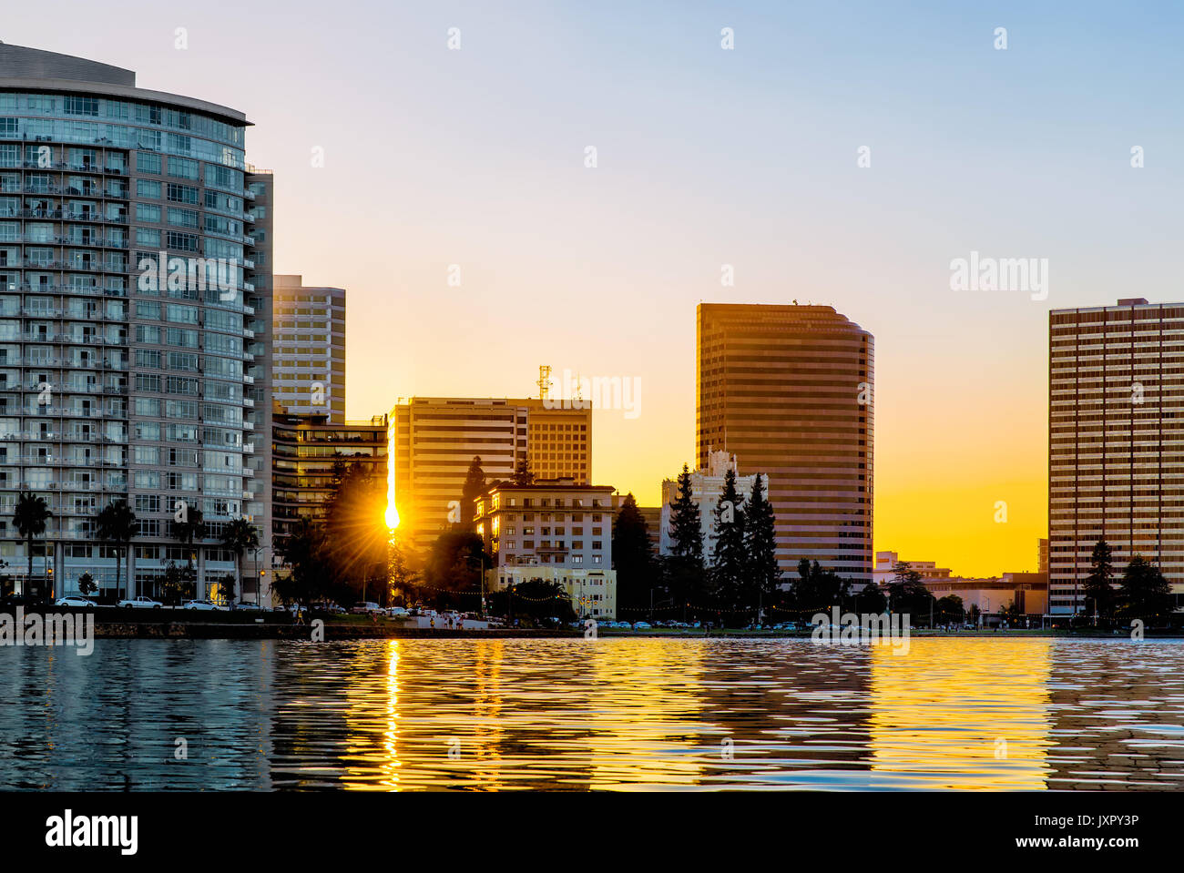 Oakland, Kalifornien Skyline entlang des Lake Merritt bei Sonnenuntergang. Zwischen den Gebäuden vom Wasser aus gesehen Sunburst. Stockfoto