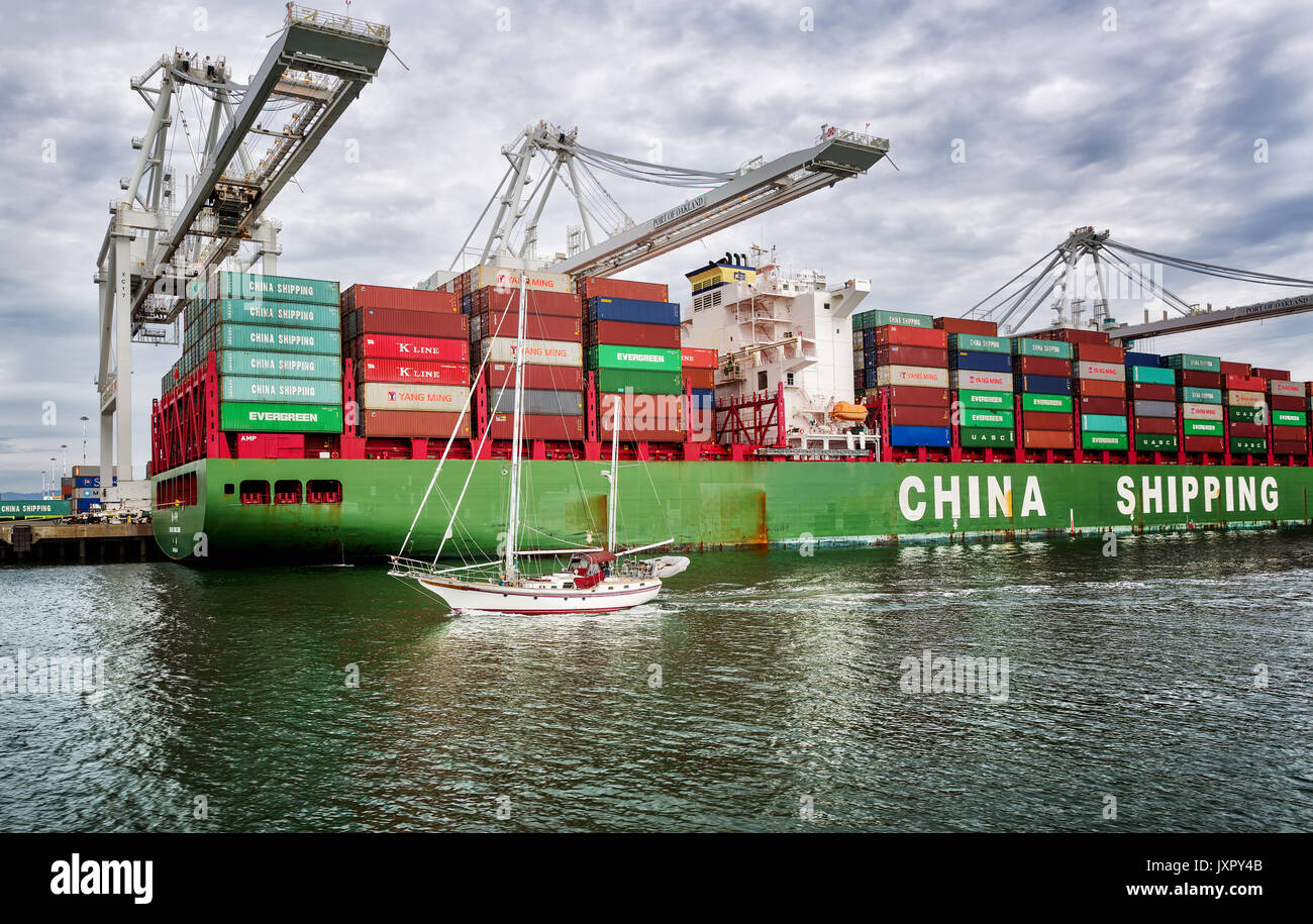 OAKLAND, CA - Jul 9, 2014: Der Hafen von Oakland in Oakland, Kalifornien. Ein Segelboot vergeht einem beladenen Frachtschiff, zeigt. Stockfoto