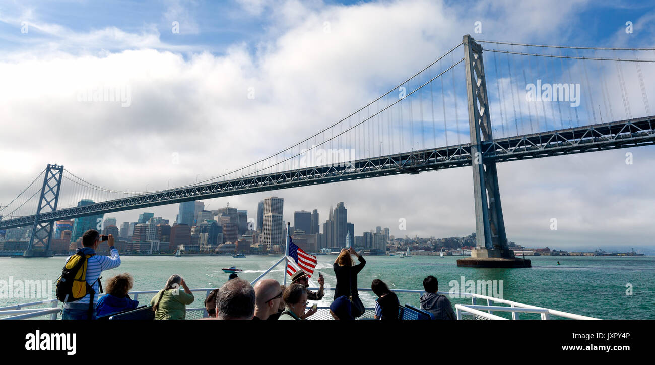 SAN FRANCISCO, Ca - Jul 9, 2014: Mit der Fähre verläuft unter der Bay Bridge mit San Francisco im Hintergrund. Passagiere nehmen Bilder der Brücke. Stockfoto