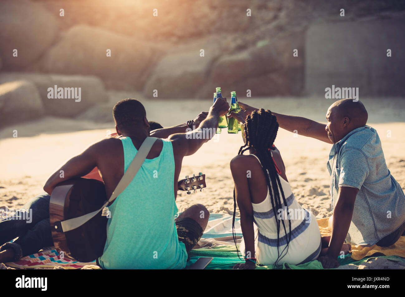 Junge Menschen Toasten mit Bierflaschen beim Sitzen am Strand. Gruppe von Freunden Getränke zusammen. Stockfoto