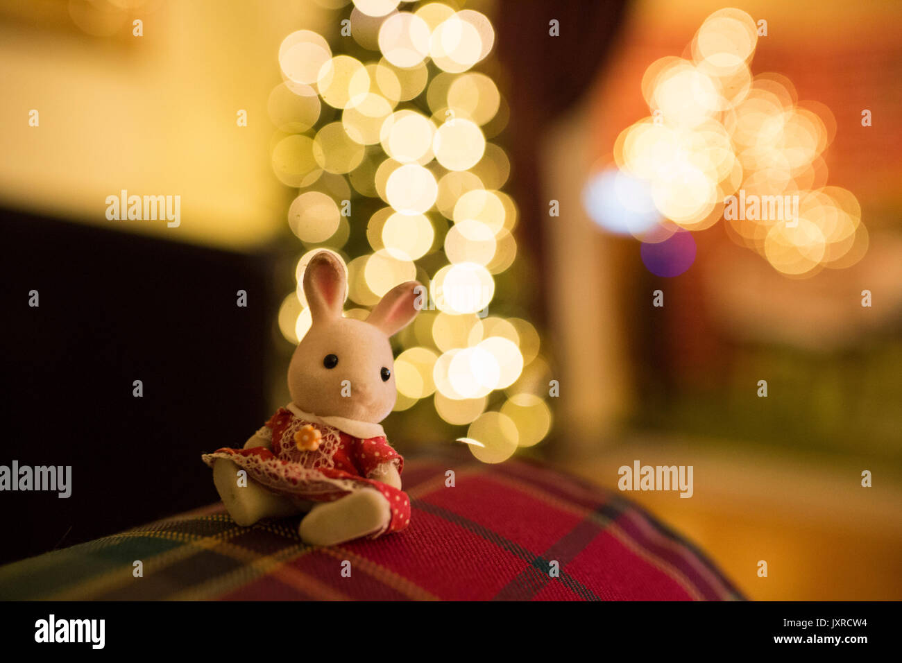 Sylvanian Familie toy Kaninchen in rot gepunkteten Kleid sitzt auf einem Sofa vor dem Weihnachtsbaum. Stockfoto