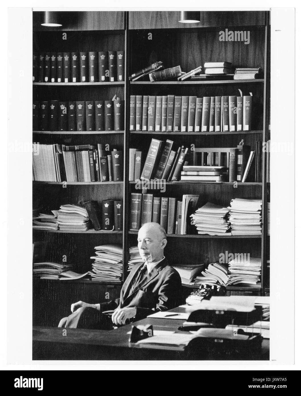 John hallock Berthel, portrait Fotografie, Sitzen, Taille, drei Viertel sehen, hinter dem Schreibtisch und vor Bücherregal, 1960. Stockfoto