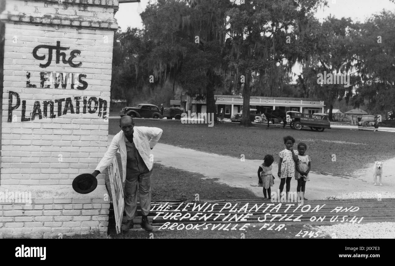 Porträt von drei afroamerikanischen Kindern und einem Mann an der Lewis Plantation in Brooksville, Florida, der Mann, der sich an einem Ziegelschild mit der Hand auf dem Rücken hinbeugte und seinen Hut im anderen hielt, während die Kinder blank aussehen, Florida, 1920. Stockfoto