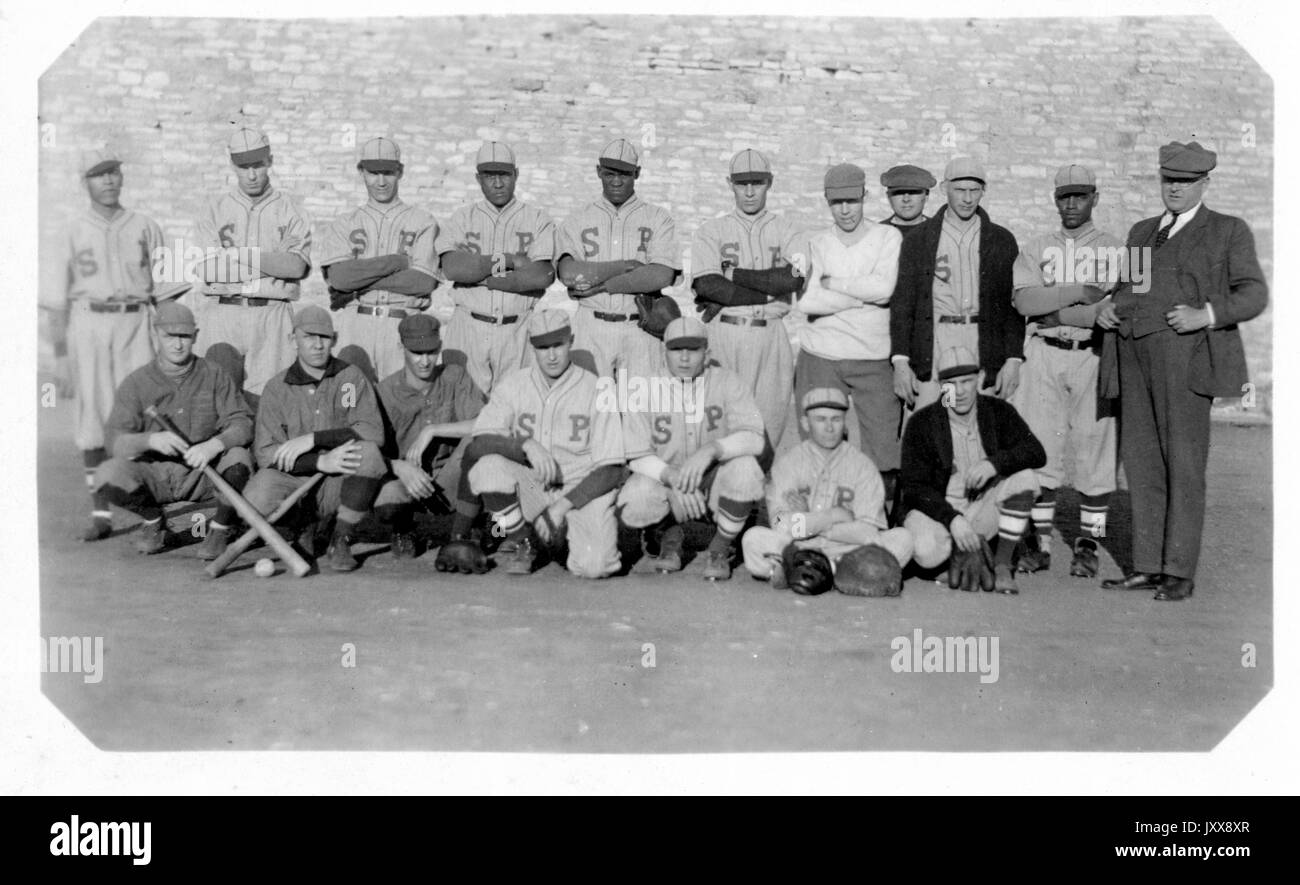 Porträt des Baseballteams des Bundesstaates Nebraska mit neutralem Ausdruck, in Uniformen, zwei der Mitglieder, die Fledermäuse halten, ihr Trainer steht rechts in einem Vollanzug, Nebraska, 1923. Stockfoto