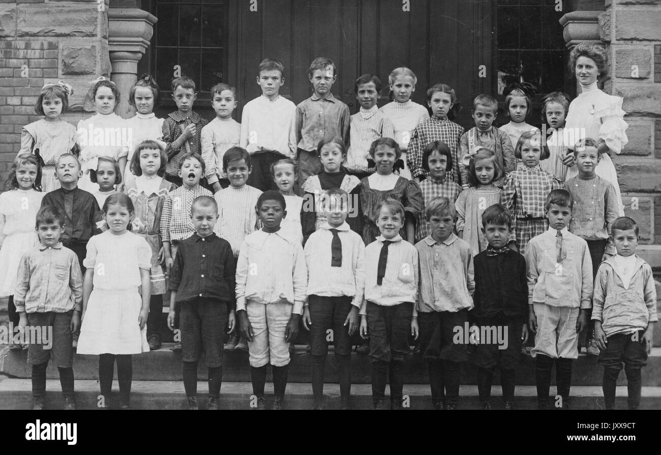 Landschaftsaufnahme in voller Länge Porträt einer Gruppe von Schülern in Reihen stehend, auf Lehrerin links, ein afroamerikanischer Junge in der ersten Reihe, alle mit lächelndem Gesichtsausdruck, 1920. Stockfoto