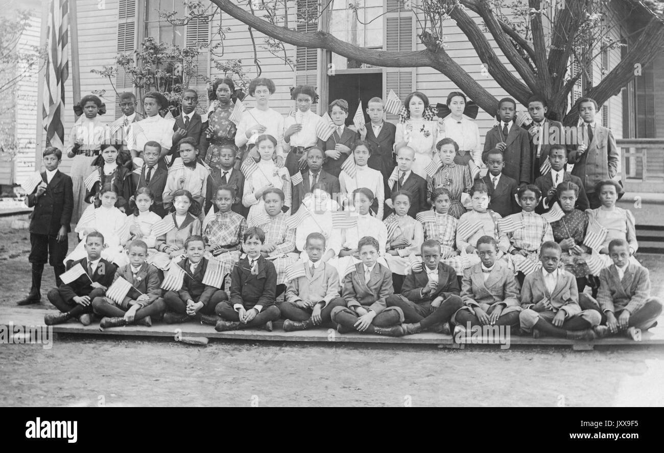 Ganzkörperbild von afroamerikanischen Schulkindern, alle in Uniform, die ersten drei Reihen sitzen, die vierte Reihe stehen, alle mit kleinen amerikanischen Fahnen, 1920. Stockfoto