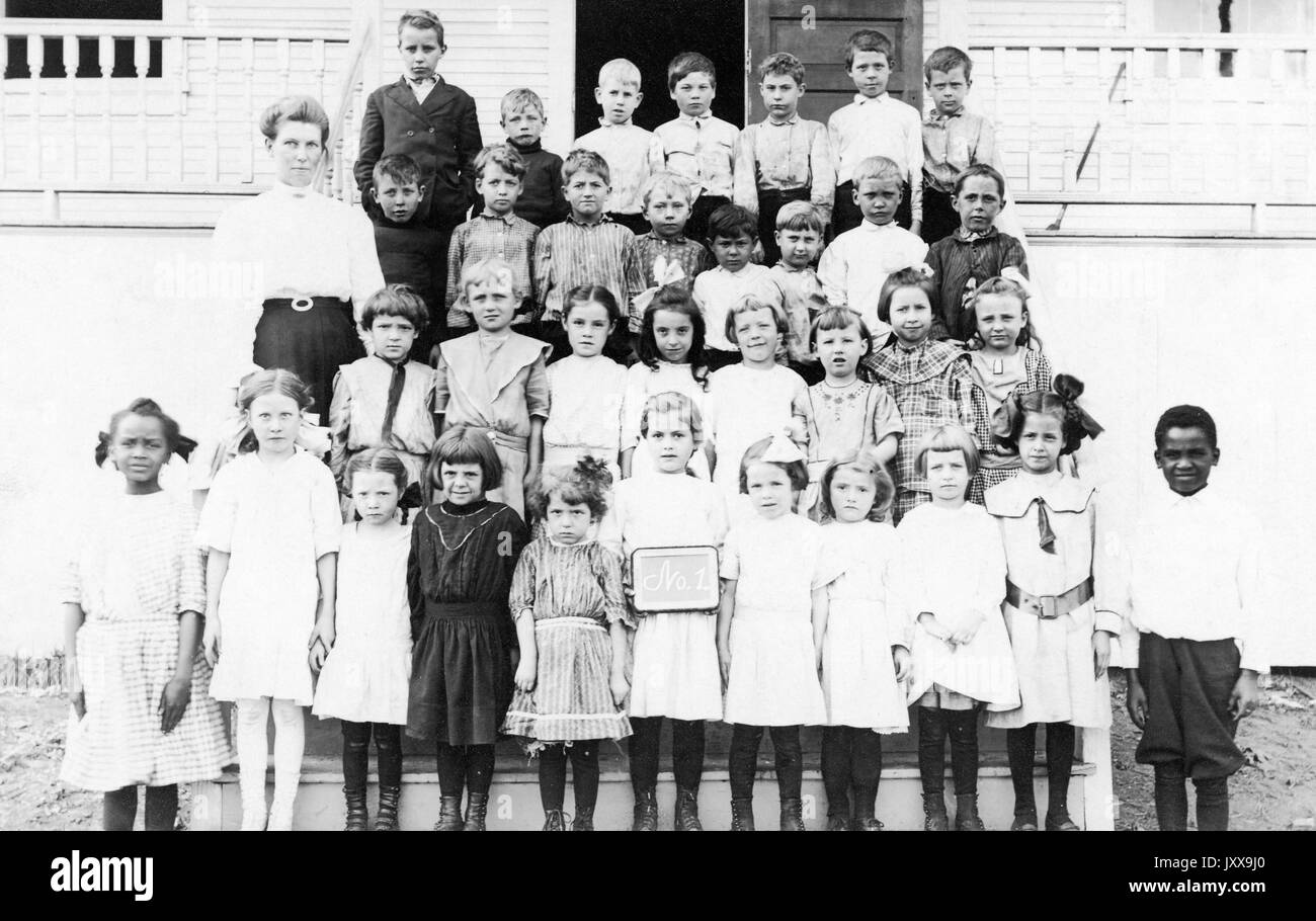 Ganzkörperportrait von kaukasischen Schulkindern, alle in Uniform, lächelnde Mimik; zwei afroamerikanische Kinder auf beiden Seiten der ersten Reihe, 1920. Stockfoto