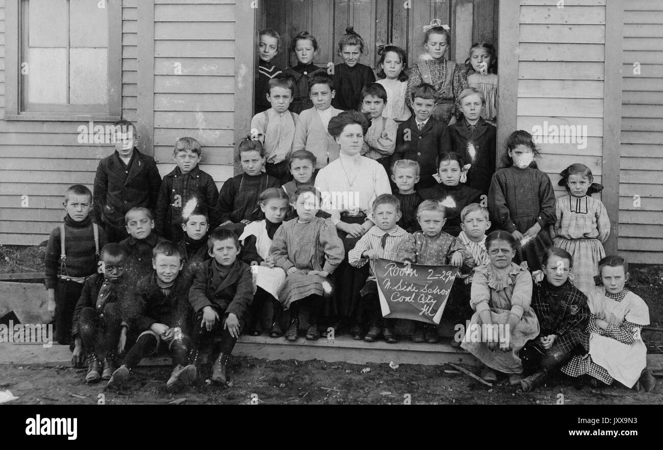 Ganzkörperaufnahme von Schulkindern, die vor dem Gebäude sitzen, ein afroamerikanischer Student unten links, 1920. Stockfoto
