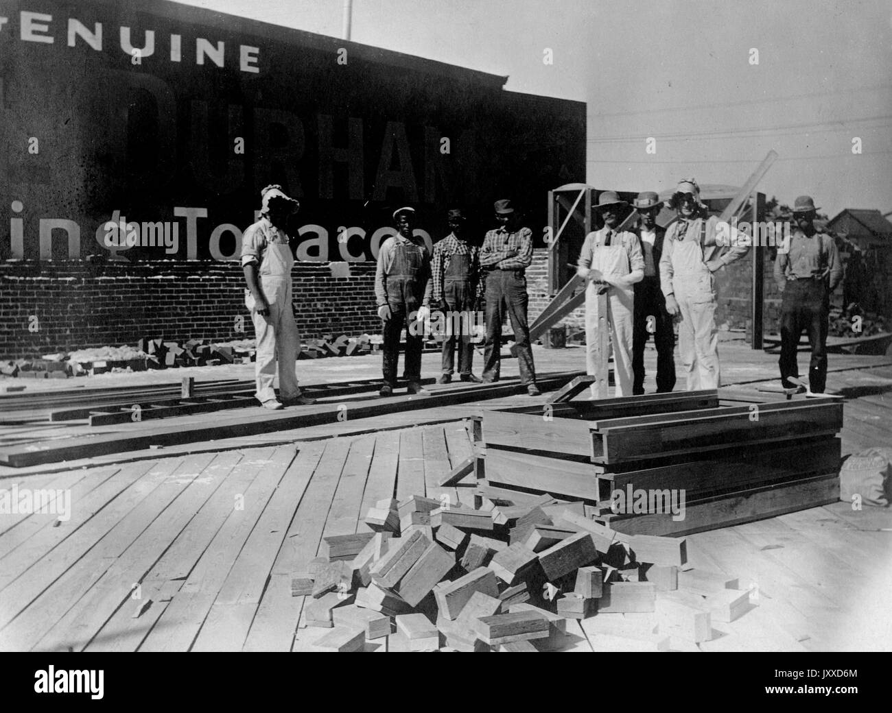 Eine Gruppe amerikanischer Bauarbeiter mit neutralem Ausdruck steht außerhalb des Gebäudes eines Tabakunternehmens auf einer Plattform, mit Haufen von Ziegeln oder Pflastersteinen vor und hinter ihnen, 1915. Stockfoto