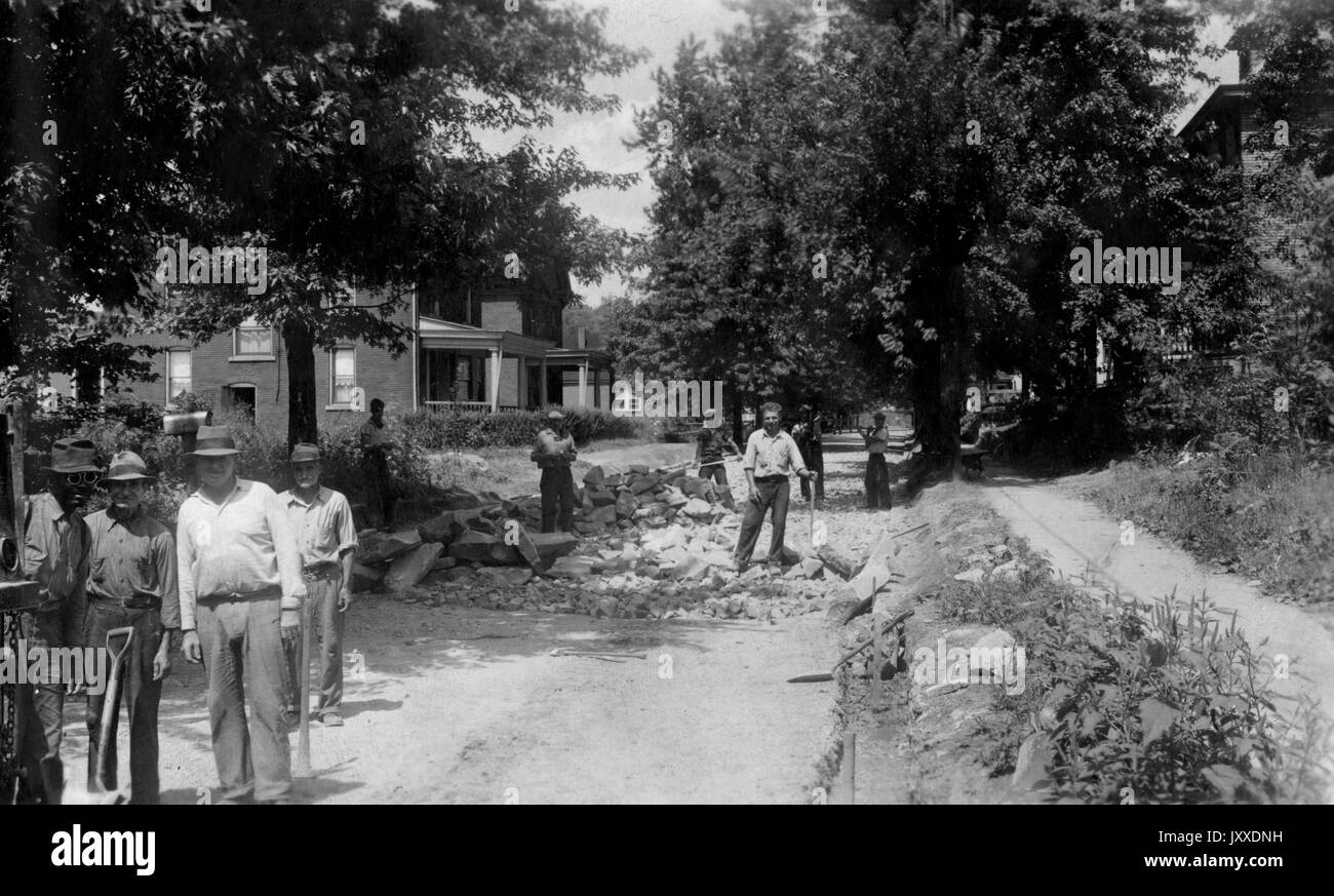 Eine Gruppe von amerikanischen Arbeiter mit neutralen Ausdrücke steht außerhalb mit Tools wie Schaufeln und Spitzhacken, vor Häuser, die in einer amerikanischen Stadt, möglicherweise North Versailles, Pennsylvania, Delaware, 1920. Stockfoto