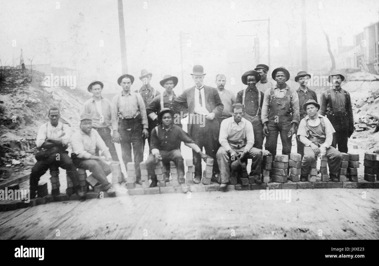 Gruppe der amerikanischen Arbeiter, darunter ein Mann in der Mitte in feiner Kleidung, erscheint Ihre überlegene, Sitzen und Stehen unter den kleinen Stapel von Backsteinen, draußen zu sein auf einem Weg, 1920 bekleidet. Stockfoto