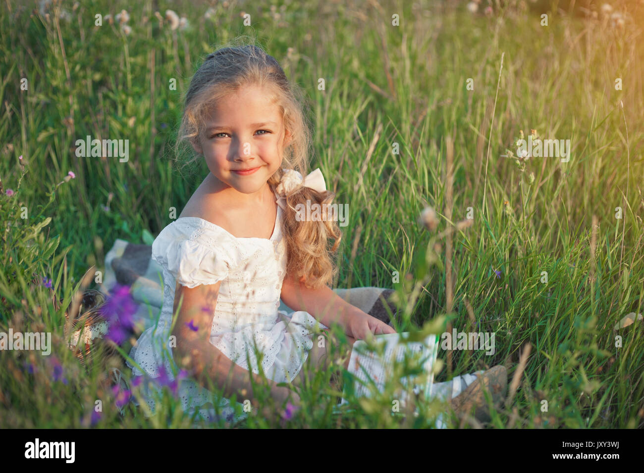 Kleines Mädchen mit einem Buch in der Hand auf einer Wiese in einem Sommer sonnigen Tag. Stockfoto