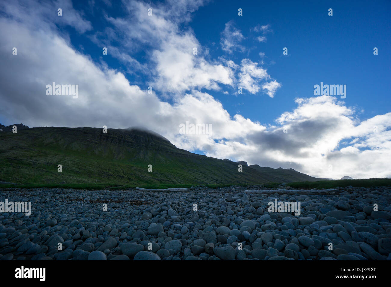 Island - intensiv grün Moos bedeckt Berg hinter Stein Feld unter blauem Himmel Stockfoto