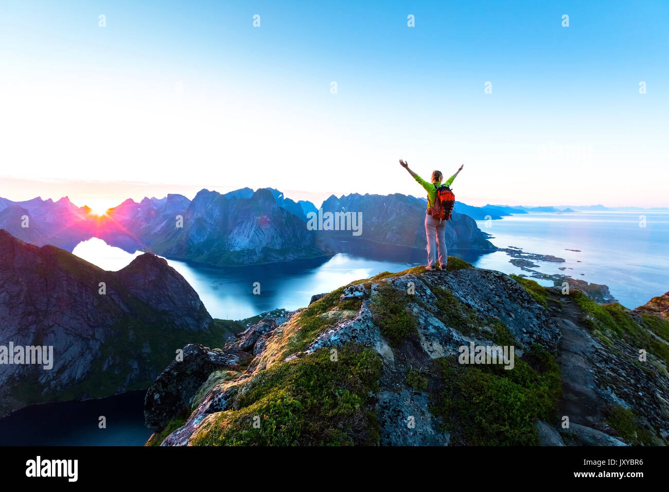 Glückliche Frau Wanderer genießen Sie einen malerischen Blick auf die Mitternachtssonne am oberen Rand Reinebringen Wanderung über Reine Dorf in der Lofoten Inseln während der arktischen Su Stockfoto