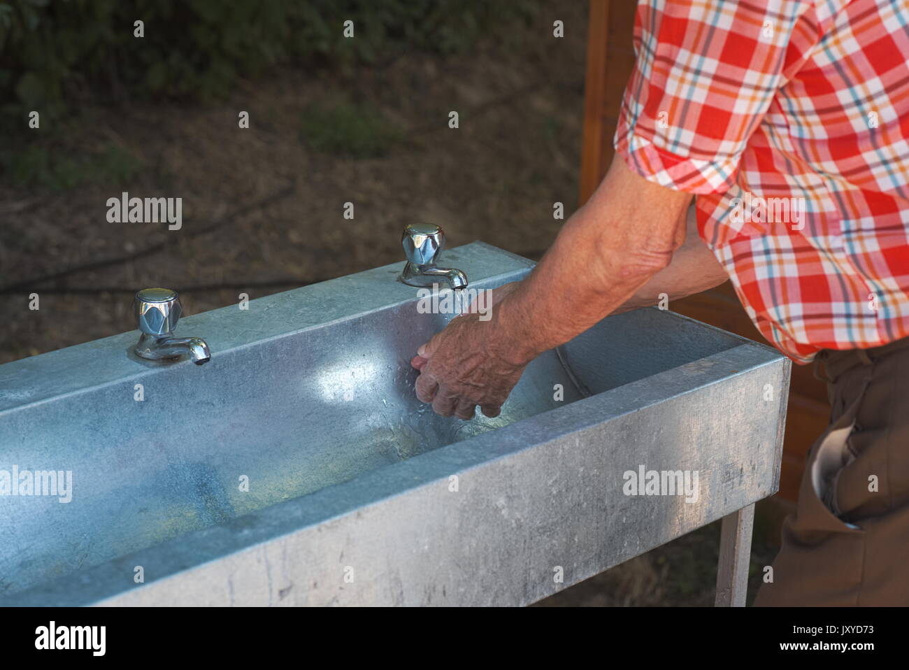 Alter Mann in kariertem Hemd waschen seine Hände im Freien Stockfoto
