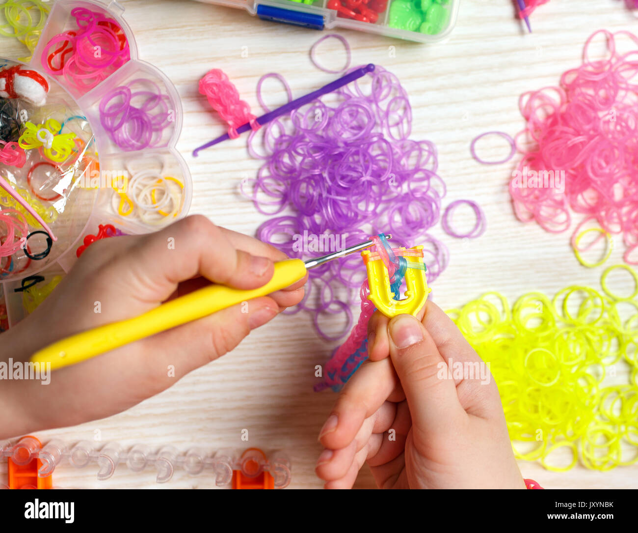 Handarbeit, Weberei, Gummi, farbige Gummibänder auf dem Tisch. Hände Mädchen Geflecht aus Gummi Stockfoto