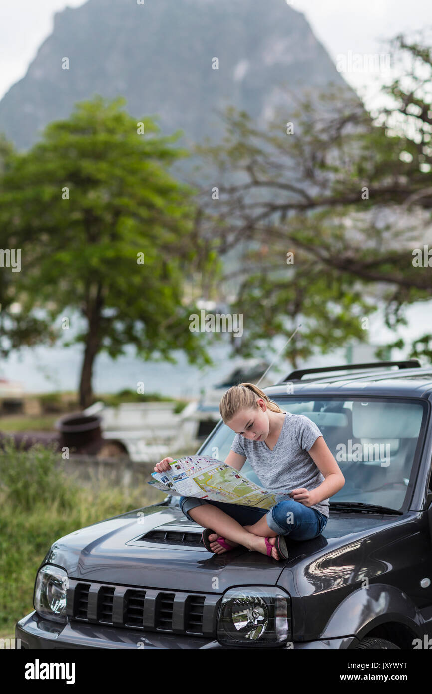 Kaukasische Mädchen sitzen auf der Motorhaube des Autos Lesen der Karte Stockfoto