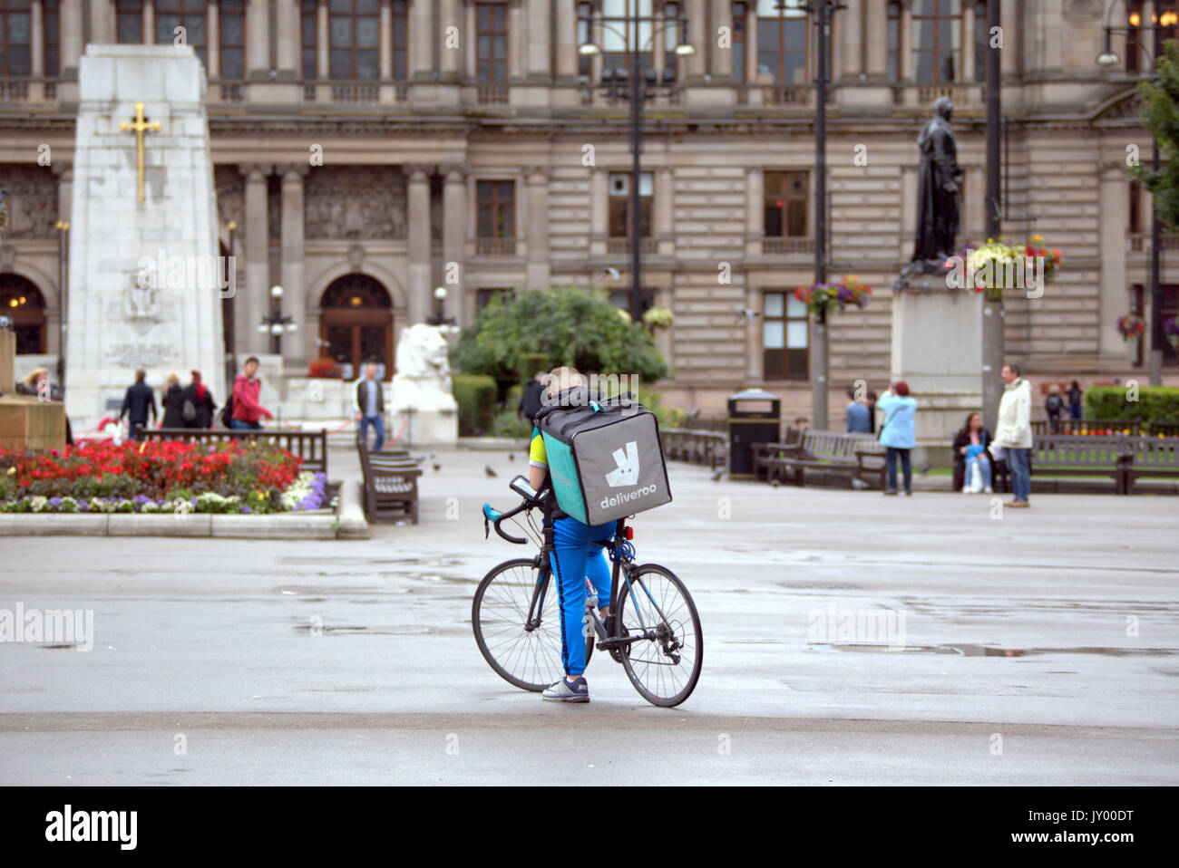 Nasse George Square Glasgow junge Mann junge Lieferung bike Radfahrer Deliveroo Lebensmittel-lieferservice texting warten auf Job, die draußen auf der Straße Straße Stockfoto