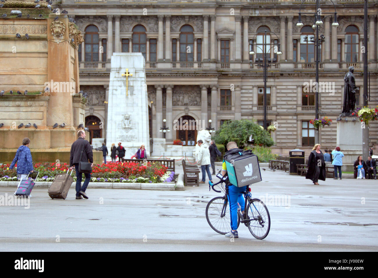 Nasse George Square Glasgow junge Mann junge Lieferung bike Radfahrer Deliveroo Lebensmittel-lieferservice texting warten auf Job, die draußen auf der Straße Straße Stockfoto