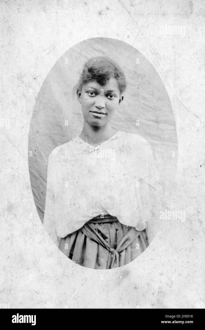 Halblanges Porträt einer jungen afroamerikanischen Frau, die mit den Armen an den Seiten steht, einen Rock und eine helle Bluse trägt, die Haare werden zurückgezogen, 1915. Stockfoto