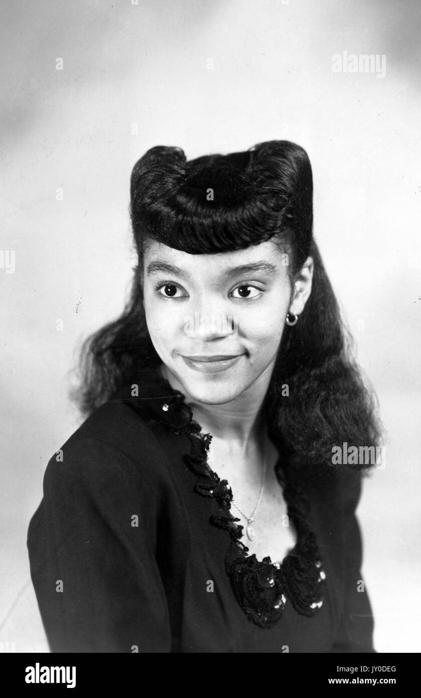 Kopfschuss einer jungen afroamerikanischen Frau, die lächelt, trägt sie eine dunkle Bluse und hat die Hälfte ihres Haares zurückgezogen, 1929. Stockfoto