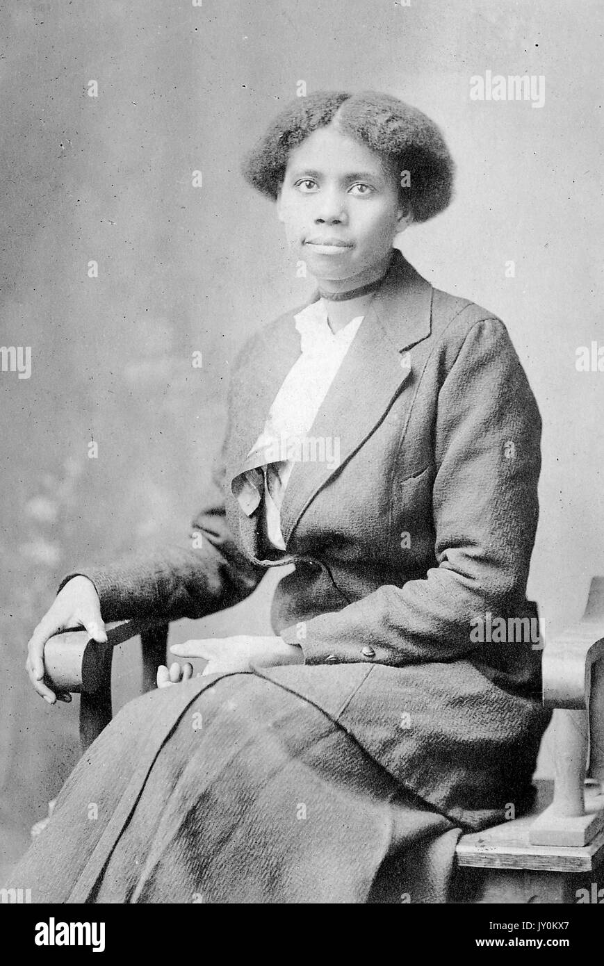 Dreiviertel sitzendes Porträt einer jungen afroamerikanischen Frau, in dunklem Kleid, dunklem Blazer und Choker, neutraler Ausdruck, 1920. Stockfoto