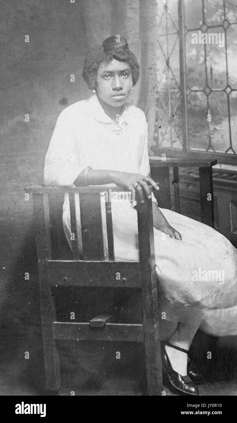 Volle Länge sitzen Porträt, junge afrikanische amerikanische Frau, tragen, leichte Kleidung und Schmuck, sitzen vor dem Fenster, 1915. Stockfoto