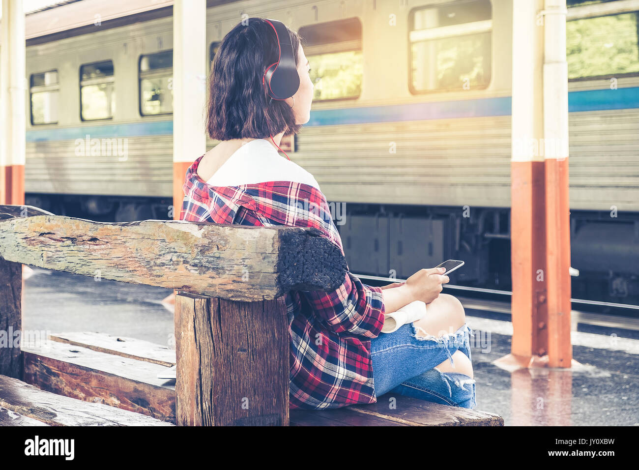 Young Travel am Bahnsteig sitzen und hören Musik ihr Zug für Reisen warten. Alleine reisen und Sommer Konzept. Stockfoto